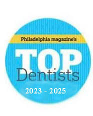 The image features a circular logo with text that reads PHILADELPHIA MAGAZINE S TOP DENTISTS in white letters on a blue background, accompanied by a small graphic of a top hat.